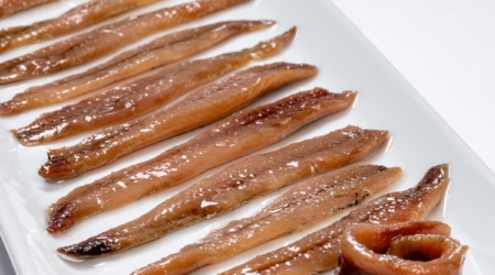 ALT: Anchoas en salazón en plato blanco, típico producto de la gastronomía española en Albergue la Casa de Gandara. Descubre la comida tradicional de Cantabria