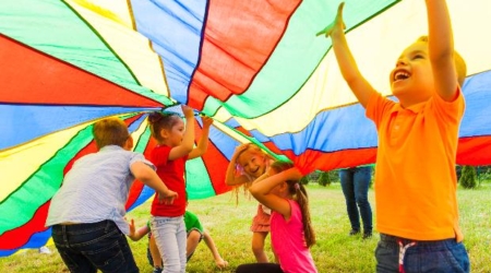 Colorido grupo de niños jugando con un paracaídas en un entorno natural, ideal para familias en Albergue la Casa de Gandara. Cómo Organizar un Campamento de Verano